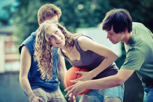 Two boys and a girl playing a game of basketball on an outdoor court.