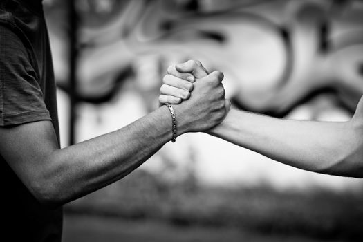 White teen and Black teen clasp hands against a wall with graffiti