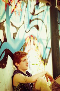 A guy relaxing leaning against a wall with graffiti