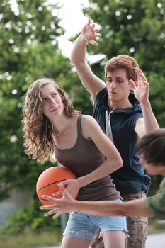 Two boys and a girl playing a game of basketball on an outdoor court.