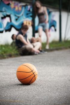 Group of friends talking and taking a break after playing basketball, focus on ball