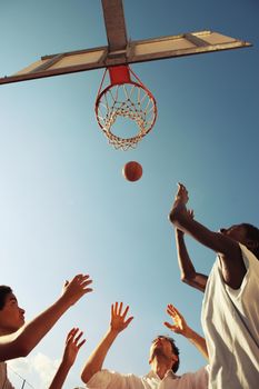 Two Afro-American boy and a man playing basketball against blue sky