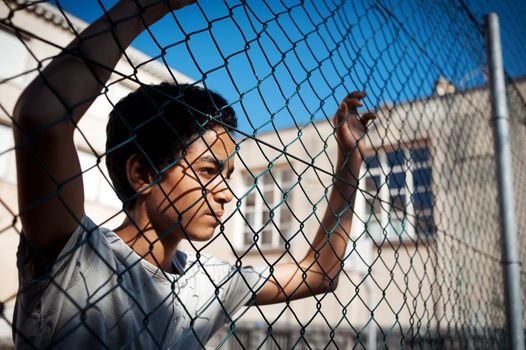 A boy looks  while leaning up against a chain link fence