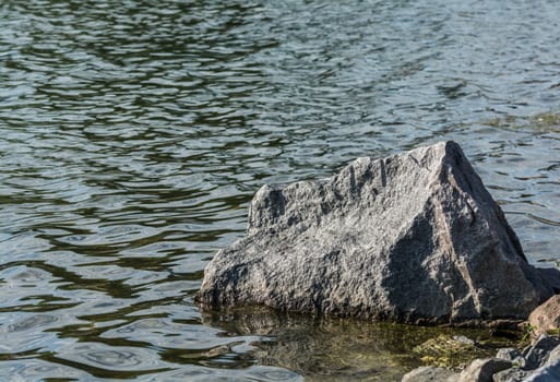 Large boulder sitting at lakeside above the surface of water