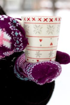 Cozy red gloves hold a mug of hot cocoa on a snowy day