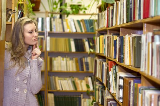 female student standing at bookshelf in old library searching for a book.