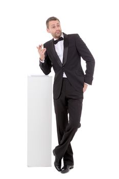 Elegant slender man in a suit and bow tie leaning nonchalantly on a white pedestal with a quizzical charismatic expression