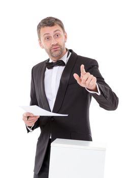 Elegant slender man in a suit and bow tie leaning nonchalantly on a white pedestal with a quizzical charismatic expression