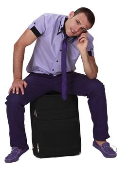 Young man sitting on a suitcase and using his mobile phone, isolated against a white background.