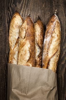 Four baguette bread loaves in paper bag on wooden background