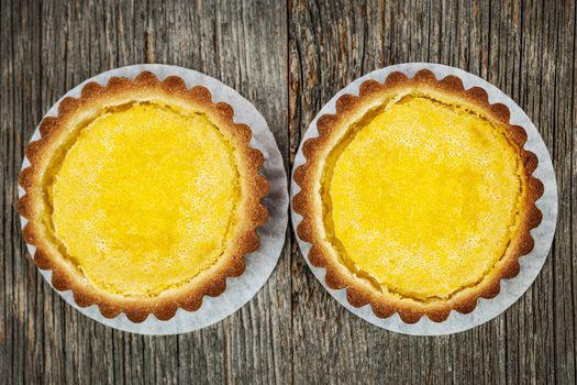 Two fresh gourmet lemon dessert tarts on wood background from above