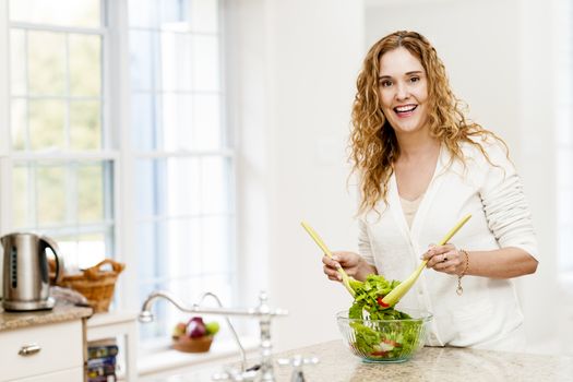 Portrait of happy woman mixing salad in kitchen at home