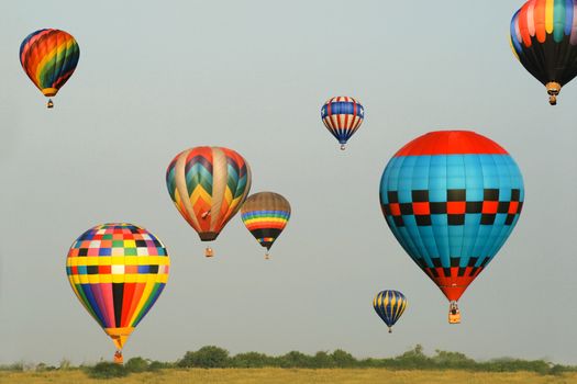 Group of eight colorful balloons in flight with blue sky background.