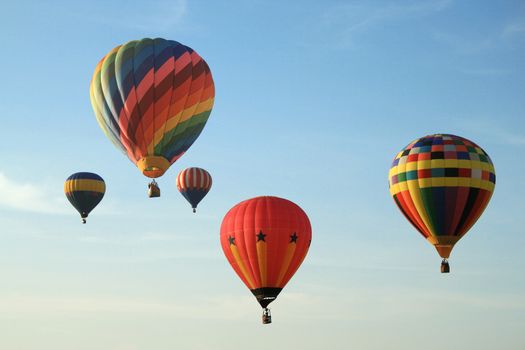 Five colorful balloons floating in blue sky.