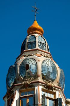 Architectural details of a cupola with round glass windows and weather vane on top.