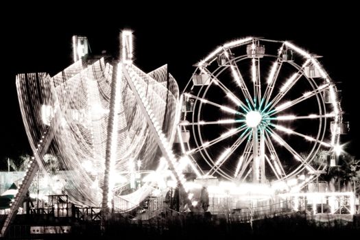 Black and white view of ferris wheel by lake illuminated at night with motion blur.