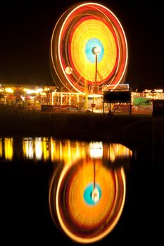 A night shot of a ferris wheel by a lake.