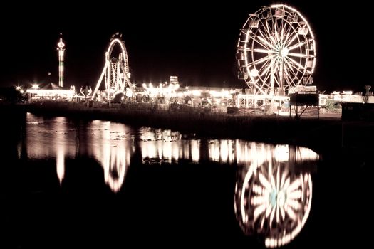 Black and white view of Ferris wheels reflecting on surface of lake at night.