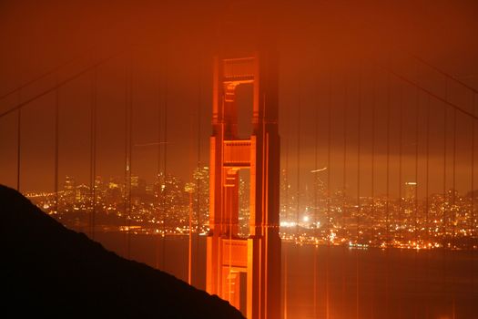 Scenic view of Golden Gate Bridge at night with fog over illuminated city in background, San Francisco, California, U.S.A.