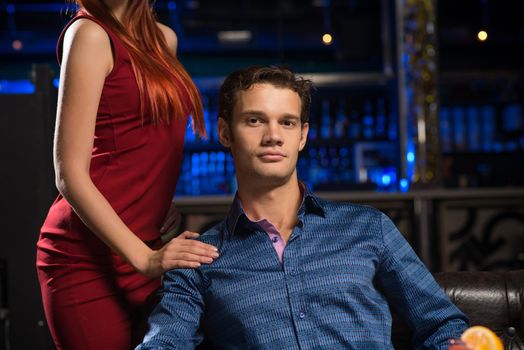 Portrait of a successful man in a nightclub, sitting on the couch, next to a woman in a red dress