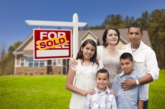 Young Happy Hispanic Young Family in Front of Their New Home and Sold For Sale Real Estate Sign.