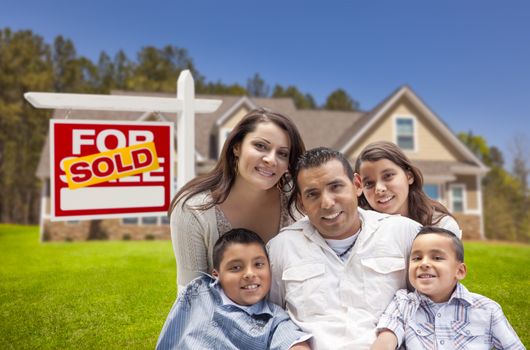 Young Happy Hispanic Young Family in Front of Their New Home and Sold For Sale Real Estate Sign.