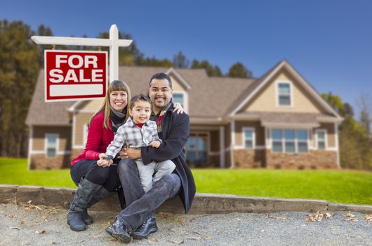 Happy Mixed Race Family in Front of Their New Home and a For Sale Real Estate Sign.