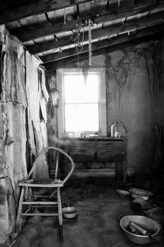 Interior of derelict gold miner's cabin at Bodie Historic Park showing broken chair, chest of drawers, metal wash basin and wooden ceiling.