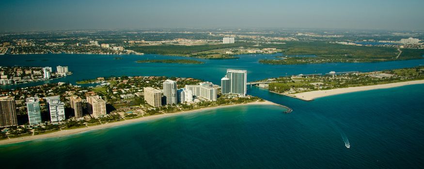 An aerial view of the seashore in Miami show deep green and blue waters.