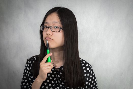 Portrait of girl deep in thought with green pen in hand on gray background