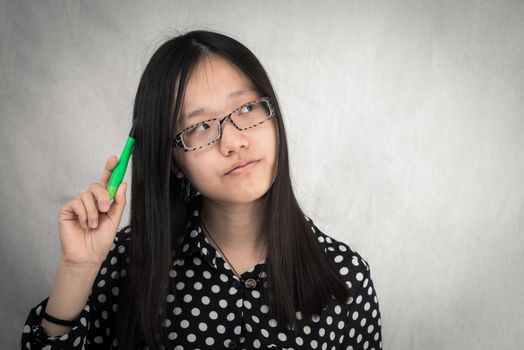 Portrait of girl deep in thought with green pen in hand on gray background