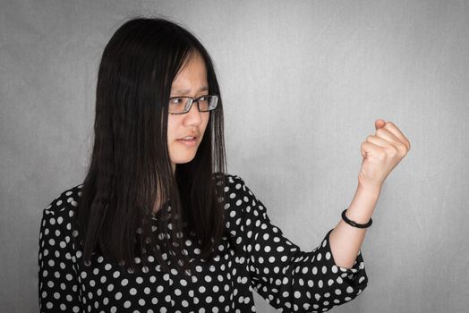 Portrait of girl clenching her fist tight in anger on gray background