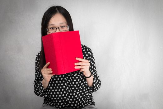Portrait of girl covering mouth with a red book on gray background