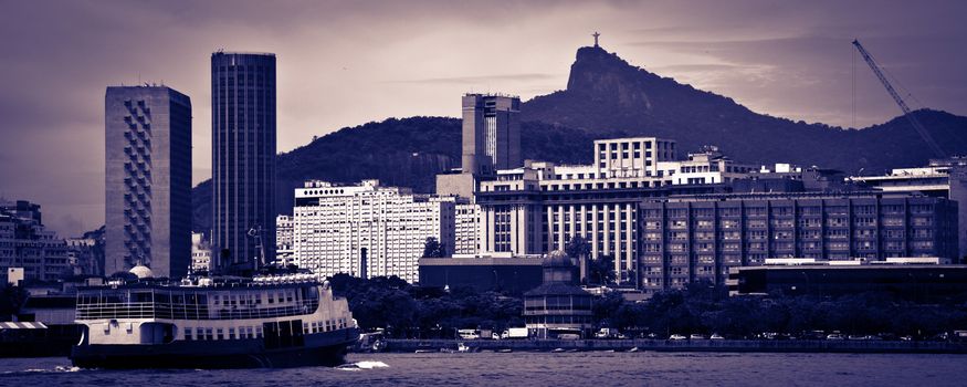 Skyline of Rio de Janeiro city with ship sailing in foreground, blue toned image.