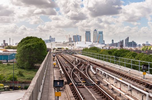 The railway tracks of Docklands Light Railway with Canary Wharf skyscrapers in the background.