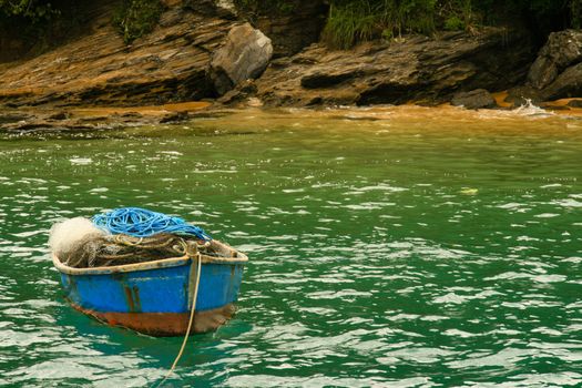 Small wooden fishing boat moored off rocky coastline, Buzios, Rio de Janeiro, Brazil