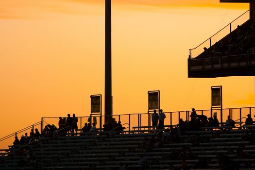 Silhouetted spectators on grandstand with colorful orange sunset background.