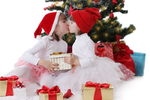 Two little sisters kissing under Christmas tree over white