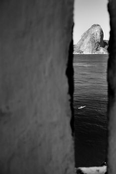 Black and white scenic view of Sugarloaf mountain viewed from gap in walls of Santa Cruz fortress, Niteroi, Brazil.