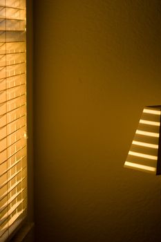 Sun shining through blinds in living room with wall in background.