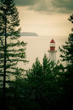 Mobile photography toned lo-fi styled image of lighthouse between lush green trees on British Columbia, Canada, West Coast north of Vancouver