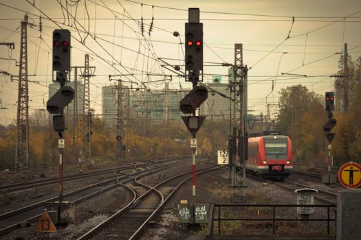 Mobile photography lo-fi styled image of a red commuter train on an urban railway track with confusing lines and overhead cables and a red signal light