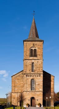 Front view of bell tower and entrance of old Catholic stone church in village town of rural country Germany, Europe under clear blue sunny sky