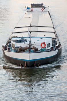 Inland waterway vessel or barge heavily loaded on transportation channel heading to deliver industrial goods