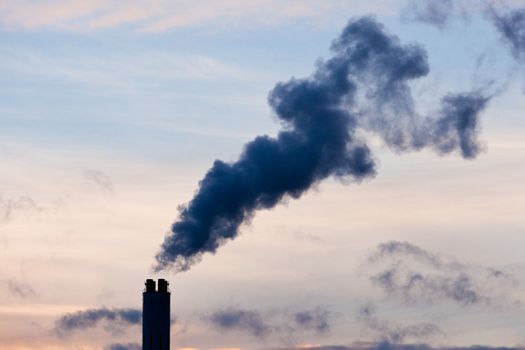 Smokestack chimney belching black smoke and pollutants in blue evening sky contributing to global warming and climate change