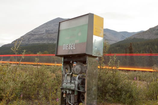 Old disused diesel pump with exposed interior parts in mountainous rural country setting and light trails of passing vehicle