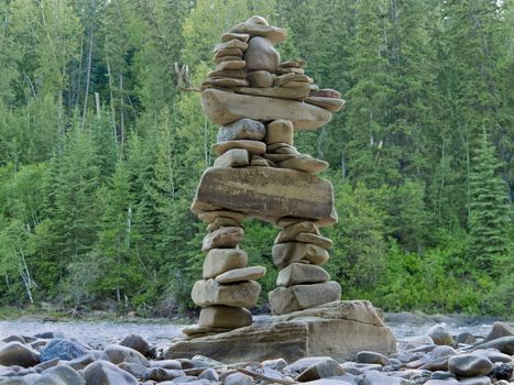 Large rocks stacked and balanced to form an Inuksuk stone landmark or cairn as a marker or monument in front of boreal forest taiga wilderness terrain