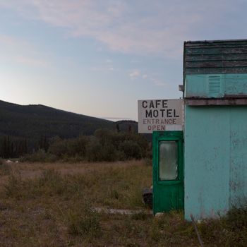 Abandoned cafe motel building with entrance door wide open in remote place with vegetation reclaiming the property