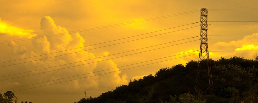 Transmission tower on hillside with sunset and cloudscape background.