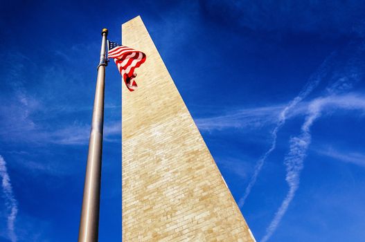 Low angle view looking to top of Washington monument with American flag, blue sky and cloudscape background.